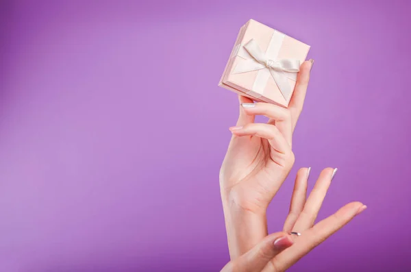 Mani femminili che tengono una piccola scatola regalo su sfondo viola . — Foto Stock