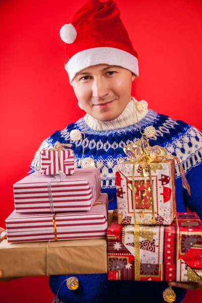 Studio shot of a young man in Icelandic sweater holding a heap of gift boxes. Christmas or New Year celebration concept. — Stock Photo, Image