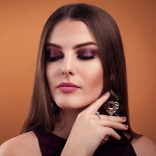 Mulher bonita maquiagem perfeita usando jóias no fundo marrom — Fotografia de Stock
