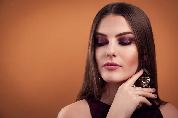 Mooie vrouw perfecte make-up dragen sieraden op bruine achtergrond — Stockfoto
