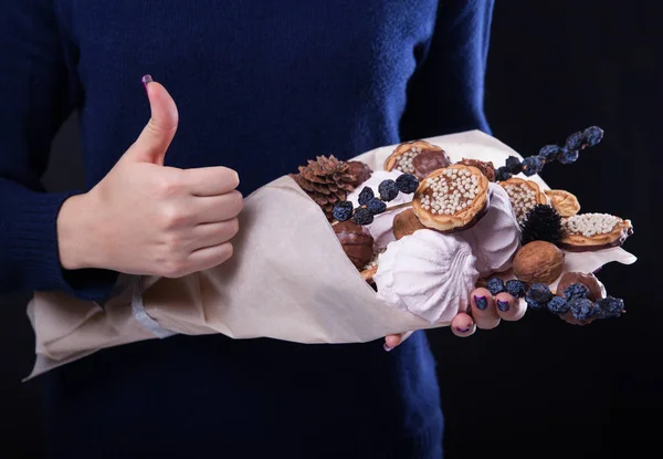 Woman holds a sweet eatable bouquet wrapped in paper on black background