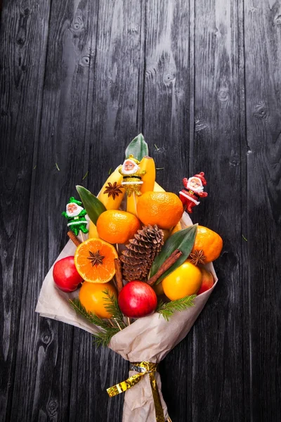Sweet eatable bouquet made of fruits wrapped in paper on black background