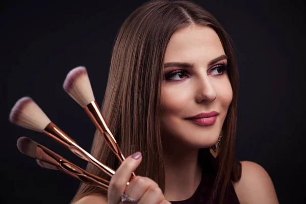 Vacker kvinna med perfekt make-up håller make-up borstar på svart bakgrund — Stockfoto