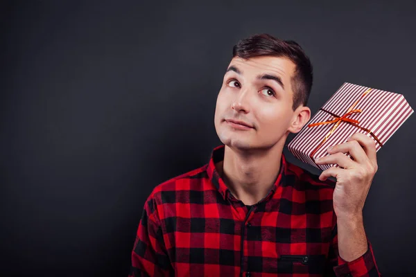 Jeune homme beau secoue une boîte-cadeau pour savoir ce qu'il y a dedans — Photo