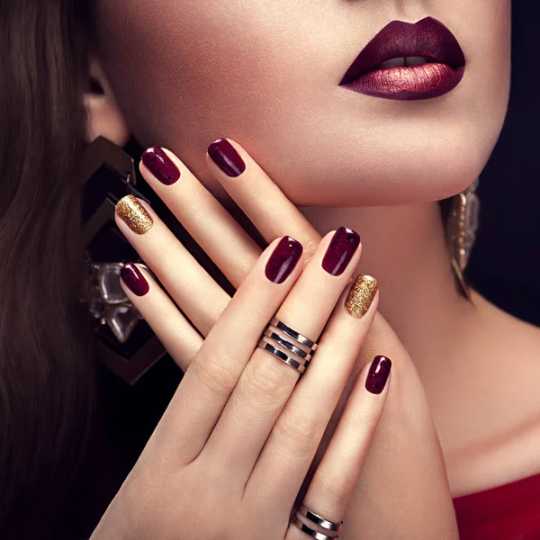 Bella donna con un trucco perfetto e una manicure bordeaux e dorata che indossa gioielli — Foto Stock