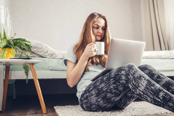 Young woman drinking coffee using her laptop in the bedroom — Stock Photo, Image