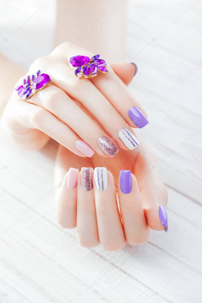 Pastel manicure with earrings on white background. Combination of purple, white, pink colors and sparkles.