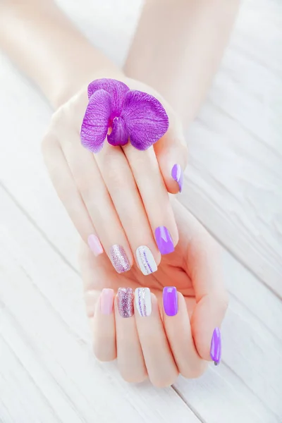 Manicure pastello con orchidea su sfondo bianco. Combinazione di viola, bianco, rosa colori e scintille . — Foto Stock