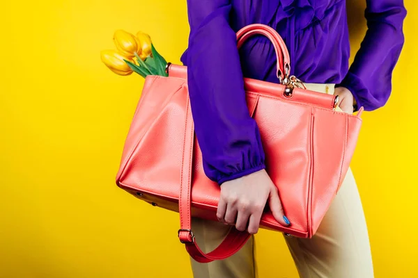 Modern and stylish look of a woman wearing spring outfit and holding a bag with yellow tulips. Studio shot — Stock Photo, Image