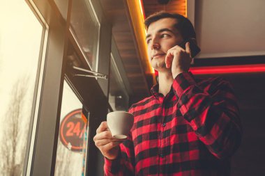 Genç adam telefonda konuşurken kafede kahve sahiptir. Sabah bir iş günü önce kahve