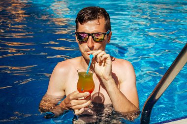 Adam yüzme havuzunda tropikal kokteyl içer. Herşey dahil konsepti