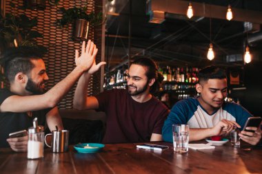 Yüksek beş arkadaşı vererek mutlu Arap genç adam. Grup lounge barda eğleniyor karışık ırk insan