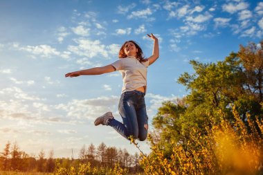 Atlama ve having fun Bahar alanına günbatımında genç kadın. Mutlu ve özgür kız doğa hoşlanır