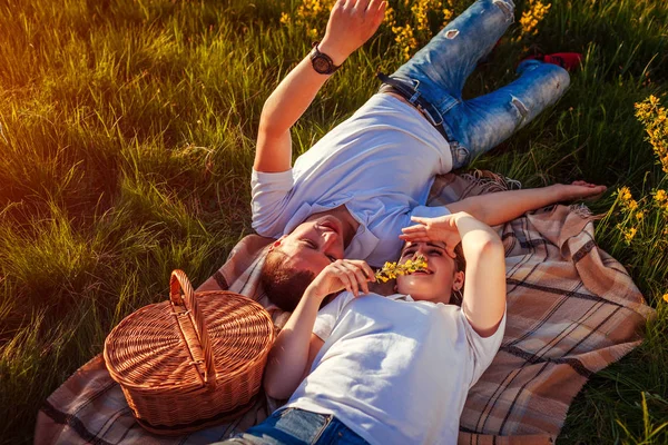 Pareja joven relajándose después de hacer un picnic. Mujer y hombre tumbados en la hierba y hablando al atardecer. Chicos relajándose. — Foto de Stock