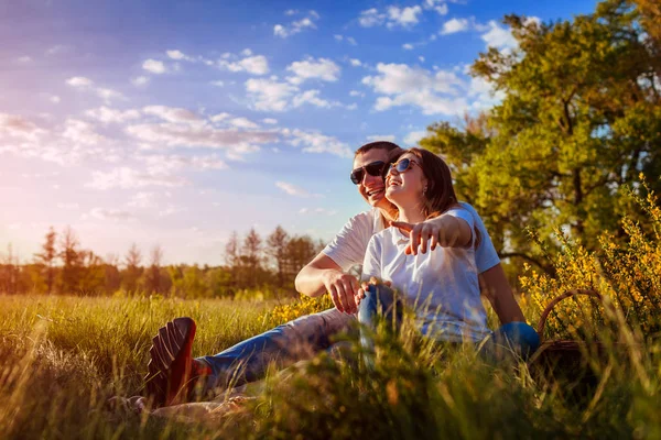 Par har roligt skratta och njuta naturen utanför. Kvinnan och mannen avkopplande efter att ha picknick i solnedgången. — Stockfoto
