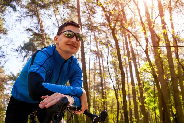 Happy young man bicyclist riding a road bike in spring forest. Man having rest