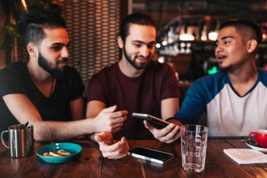 Grup telefon kullanarak ve lounge barda konuşurken karışık yarış genç adam. Orta Doğu arkadaşlar kafede kahve içip eğleniyor