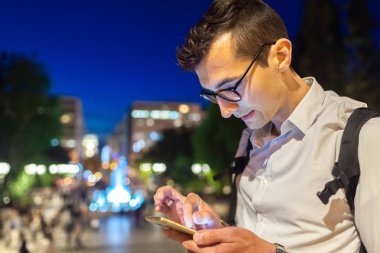 Atina, Yunanistan 'da gece vakti akıllı telefon kullanan bir adam. Park 'ta mesaj yazan adam