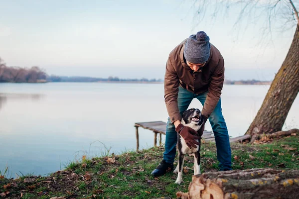 Мужчина играет с собакой в осеннем парке у озера. Счастливое домашнее животное, весело гуляющее на свежем воздухе — стоковое фото