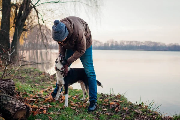 Man playing with dog in autumn park by lake. Happy pet having fun walking outdoors — Stock Photo, Image