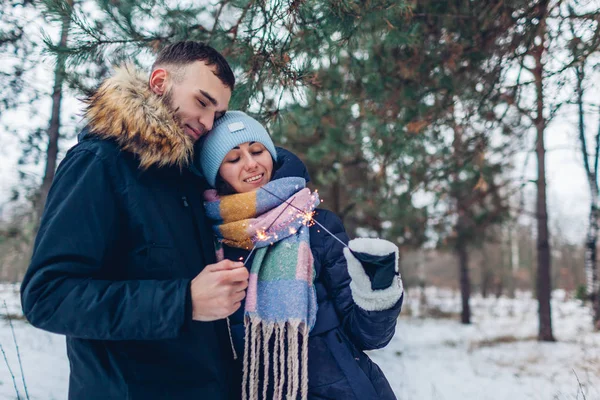 Casal amoroso queimando faíscas na floresta de inverno. Conceito de Natal e Ano Novo. Pessoas que celebram férias — Fotografia de Stock