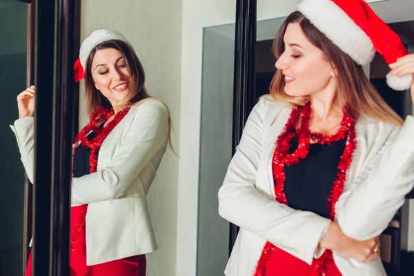 Moda de festa de Ano Novo ou Natal. Mulher verificando roupa olhando para o espelho, vestindo o chapéu do Papai Noel — Fotografia de Stock