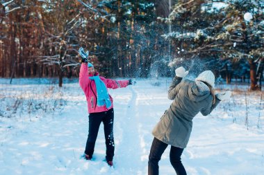 Kış ormanında kartopları oynuyor. Aile annesi ve kızı dışarıda kar atarken eğleniyor.