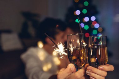 Noel ve yeni yıl partisi konsepti. Birbirine aşık bir çift, yılbaşı ağacını şampanyayla aydınlatarak havai fişek yakıyor..
