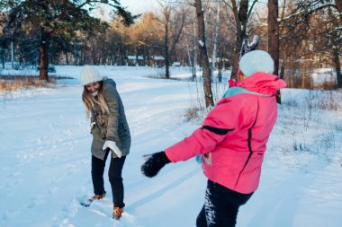Kış ormanında kartopları oynuyor. Aile annesi ve kızı dışarıda kar atarken eğleniyor.