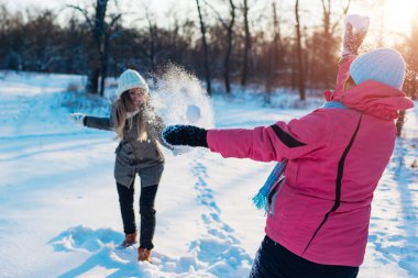 Kış ormanında kartopları oynuyor. Aile annesi ve kızı dışarıda kar atarken eğleniyor.