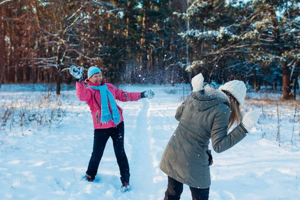 Bolas de nieve jugando en el bosque de invierno. Familia madre e hija divirtiéndose tirando nieve al aire libre — Foto de Stock