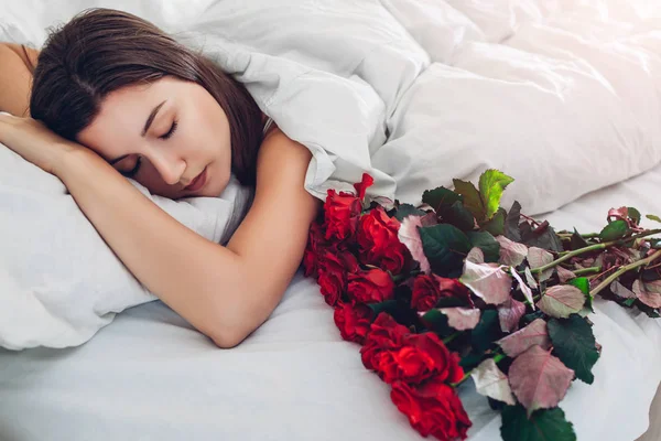 Valentijnsdag. Vrouw slapend bij boeket rode rozen in bed thuis. Vriend of echtgenoot gaf bloemen. Verrassing — Stockfoto