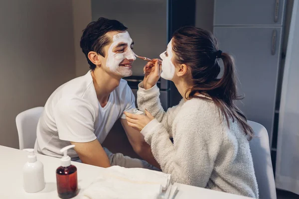 Femme qui applique un masque d'argile sur le visage de son mari. Jeune couple aimant prendre soin de la peau à la maison. Une routine saine — Photo