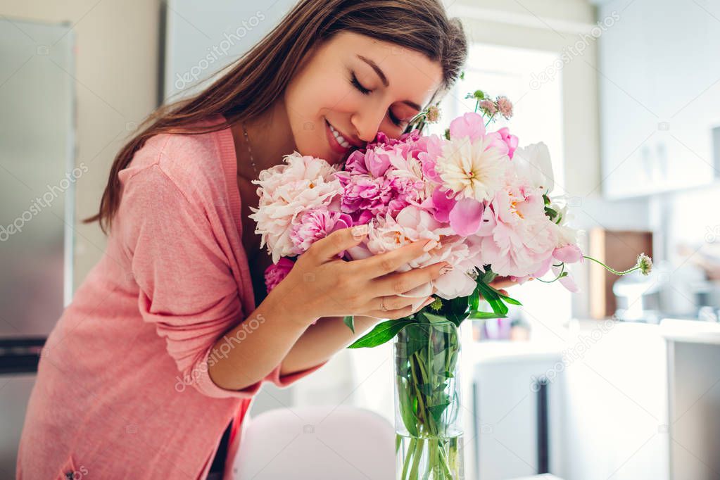 Womens day. Woman smelling bouquet of peonies. Housewife enjoying decor and interior of kitchen. Gift from husband