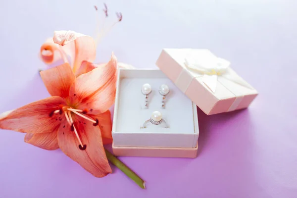 Conjunto de joyas de perlas en la caja de regalo con flores. Pendientes y anillo con lirio sobre fondo púrpura. Accesorios — Foto de Stock