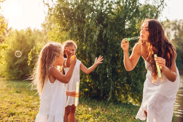A mãe ajuda filhas a soprar bolhas no parque de verão. Crianças se divertindo brincando, pegando bolhas. Dia das mães — Fotografia de Stock
