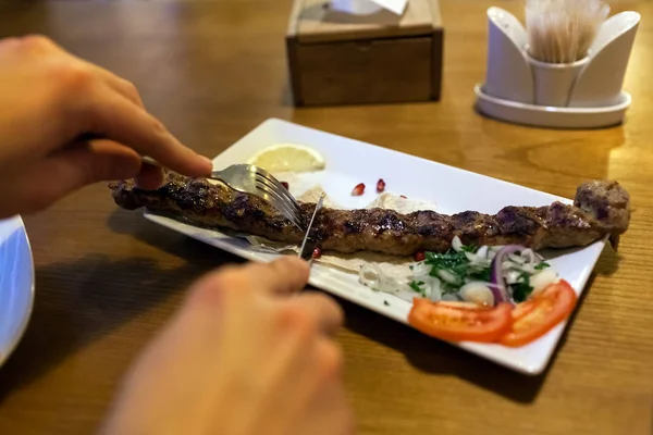 Lula kebab meat dish with vegetables served in restaurant on wooden table. Man cutting and eating barbecue food — 스톡 사진