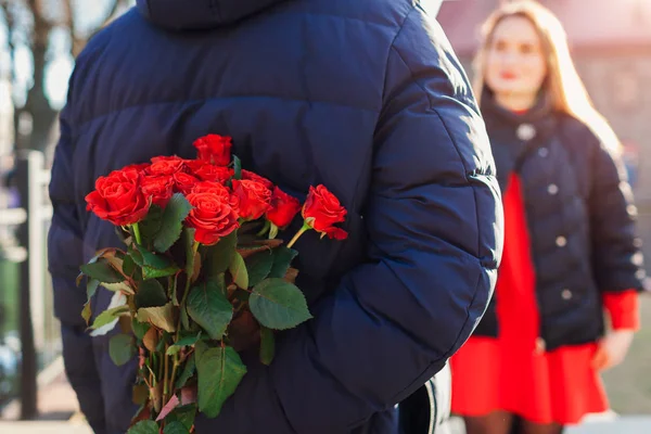 Розы на День Святого Валентина. Мужчина, прячущий букет цветов от подружки за спиной на свидании на улице. Женский день — стоковое фото