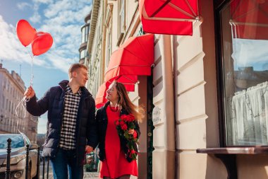 Sevgililer Günü çifti. Kadın ve erkek şehir caddesinde çiçek ve balonlarla koşuyorlar..