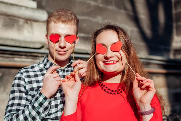 Valentines day photo booth props. Man and woman hiding eyes behind red hearts. Couple having fun
