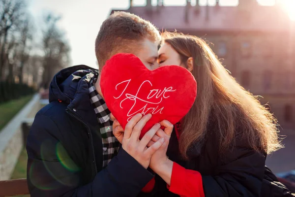 Valentinstag-Kuss. Mann und Frau verstecken sich hinter herzförmigen Kissen mit dem Schriftzug Ich liebe dich im Freien. — Stockfoto