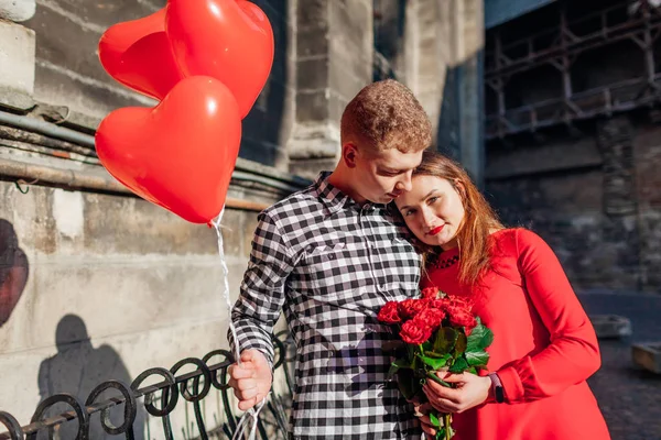 Walentynki zakochanej pary. Mężczyzna i kobieta przytulający się z bukietem kwiatów z balonami na ulicy miasta. — Zdjęcie stockowe