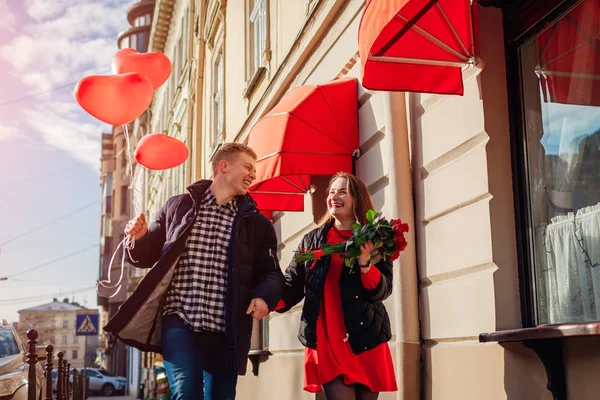 Valentijnsdag koppel. Man en vrouw rennend met boeket rozen bloemen en ballonnen op straat. — Stockfoto