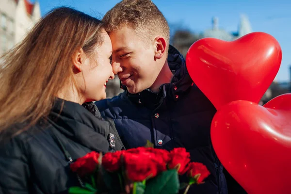 Walentynkowa randka. Mężczyzna i kobieta całujący się w mieście. Para spacerująca z kwiatami róż i balonami — Zdjęcie stockowe