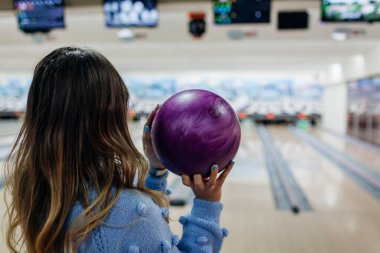 Bowling maçı. Kadınlar kulüpte bowling oynarken eğleniyor. Topu tutan kız fırlatmaya hazır ve ekrana bakıyor.