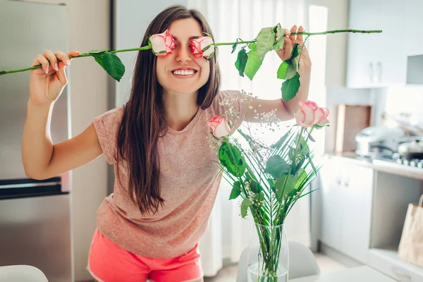 Kobieta wkłada róże do wazonu i bawi się przykrywając oczy kwiatami. Gospodyni domowa dbająca o przytulność w domu — Zdjęcie stockowe