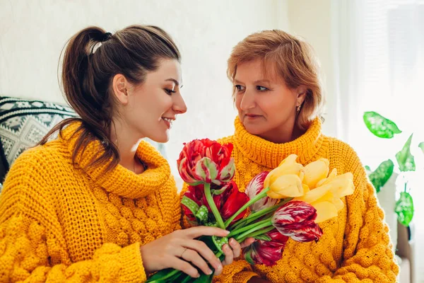 Dia das mães, dia das mulheres. Filha dando a sua mãe tulipas flores em casa como presente vestindo camisolas semelhantes — Fotografia de Stock