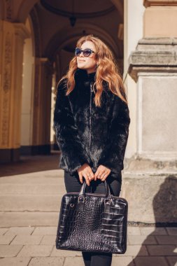 Kadın modası. Kürklü gözlüklü şık bir kadın sokakta el çantası tutuyor. Bahar kıyafeti. Dışarıdaki genç kızın portresi.
