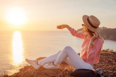 Yunanistan 'ın Santorini adasındaki Ege Dağı' nın arka planında telefonla selfie çeken bir turist. Seyahat eden bir kadın.