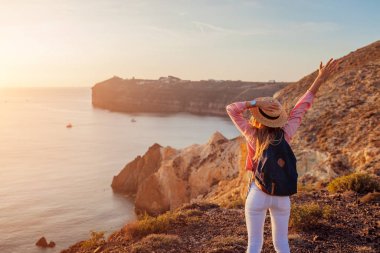 Yunanistan 'ın Ege Denizi Santorini adasındaki White Beach' te yürüyüş yapan gezgin manzaranın tadını çıkarıyor. Sırt çantalı kadın mutlu kollarını kaldırdı. Yaz turizmi